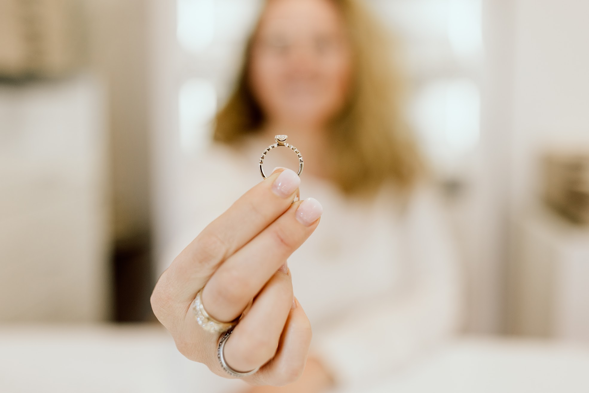 Eine Person ist im Hintergrund verschwommen. Sie hält einen Verlobungsring mit einem Diamanten in die Kamera.